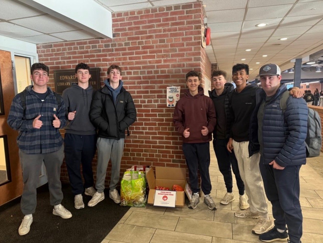 Group of nine people standing together in front of a brick wall indoors, posing for a photo