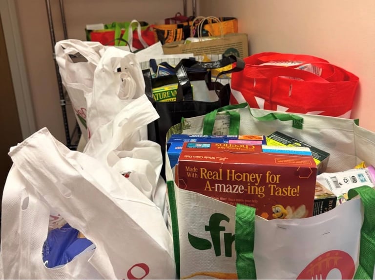 Cluttered storage area with overflowing white plastic bags, food boxes, red container, and miscellaneous household items stacked together